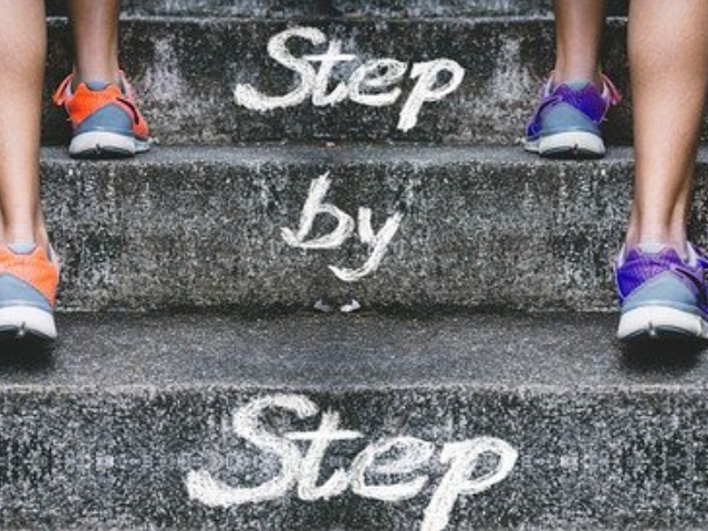 階段を歩く人の足とstep by stepの文字